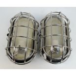 A pair of large oval bulkhead lights with clear glass and protective cage, height 32cm.