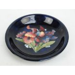 MOORCROFT; An "Orchid" pattern tube lined decorated circular shallow bowl on dark blue ground,