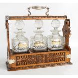 An Edwardian carved oak and silver plated three bottle tantalus with three square section decanters,