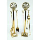 A pair of brass companion sets with cast foliate scroll decorated finials, height 61cm.