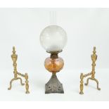 A pair of brass andirons with urn shaped finials and a Victorian oil lamp with amber glass