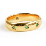 An 18ct yellow gold band set with three small green stones, size Q, hallmarked for Glasgow 1919,