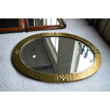 An Arts and Crafts hammered brass framed oval bevelled wall mirror decorated with fleur de lys