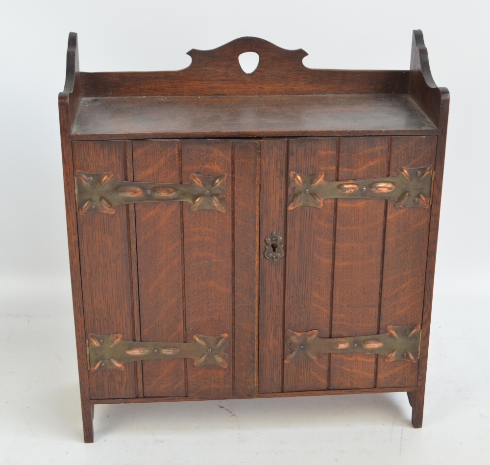 An oak Arts and Crafts smoker's cabinet with decorative copper hinges to the two doors,