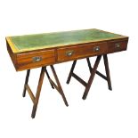 A reproduction campaign desk with three frieze drawers raised on folding trestle supports,