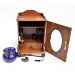 An early 20th century oak smoker's cabinet containing a tobacco jar and cover and various pipes.