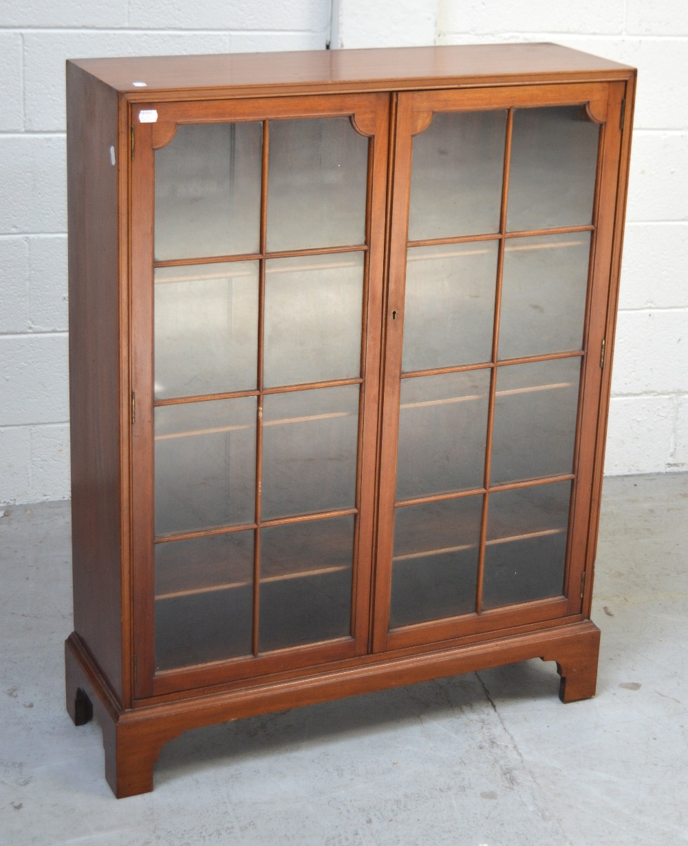 An Edwardian mahogany two-door glazed bookcase with three shelves, raised on bracket supports,