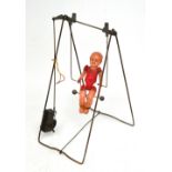 A c1950s wind-up plastic doll on metal-framed swing.