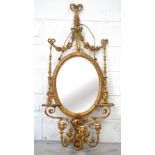 An early 19th century oval gilt mirror with ribbon and floral swags to top supported on cherub and