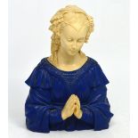 A plaster bust of a young woman in blue painted gown in prayerful pose.