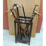 An oak four section stick stand with drip tray containing a collection of walking sticks including