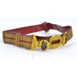 A late 19th century crimson leather belt with gold coloured thread decoration and brass buckle,