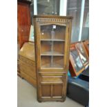 A reproduction oak freestanding corner cupboard with glazed upper section and cupboard below.