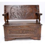 An early 20th century oak monk's bench with carved foliate scroll motifs to top and front,