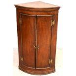 A Georgian oak bow-front corner cabinet with pair of cupboard doors and brass furniture,