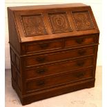 An early 20th century oak bureau with panel carved fall-front above two short and three long