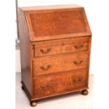 An early 20th century oak bureau, the fitted fall-front desk sits above three long drawers,