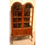 An early 20th century walnut two-door glazed display cabinet of twin dome form, three fixed shelves,