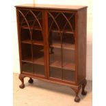 A 1920s mahogany two-door glazed bookcase with adjustable shelves, raised on ball and claw supports,