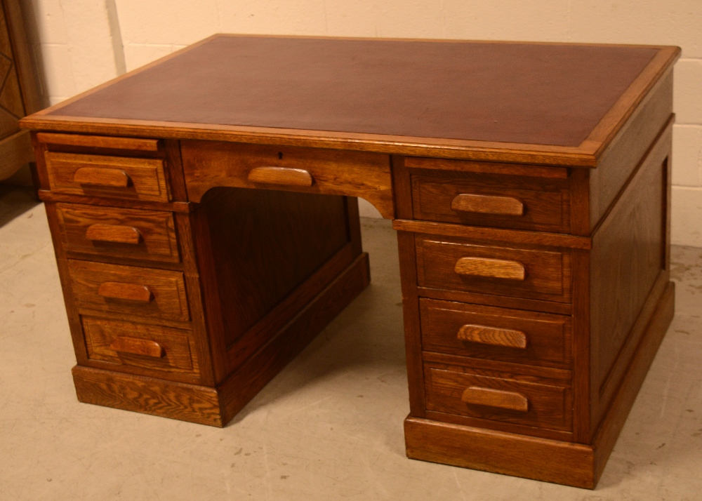 A c1930s oak kneehole desk, one central drawer with four drawers to either side on a plinth base.