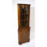 A reproduction walnut freestanding corner cupboard with single glazed door enclosing three shelves