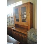 A contemporary stripped and waxed pine dresser with twin glazed doors above cupboard base,