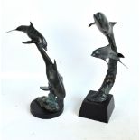 A pair of decorative metal sculptures of dolphins, one raised on a square section base,