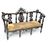 A Victorian carved salon settee elaborately carved with arabesque decoration to the centre,