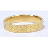 A 9ct yellow gold hinged snap bangle with upper panel engraved with flowers,