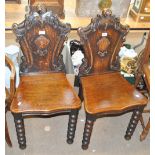 A pair of Victorian carved oak hall chairs, decorated with foliate scroll motifs to the back,