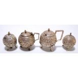 An Indian white metal four piece cruet of spherical form with repoussé decoration of scrolling