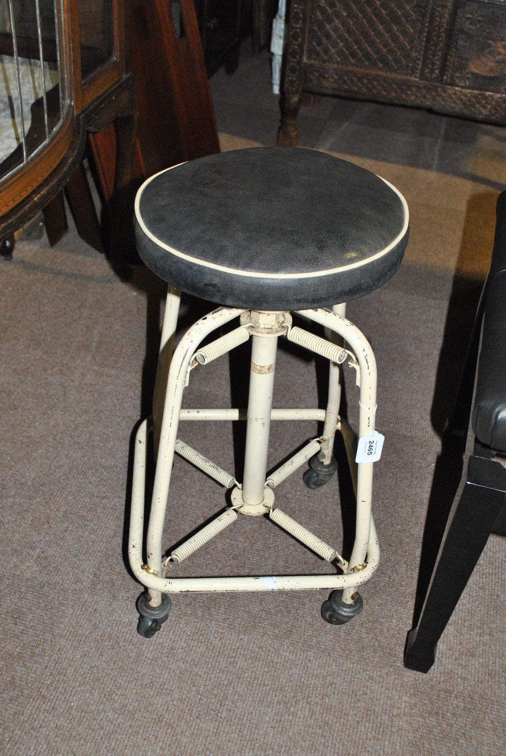 A vintage spring tubular framed cream painted stool with adjustable black leather seat,
