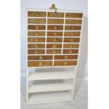 A cream painted multi-drawer chest oft twenty-five small drawers with brass recessed handles and