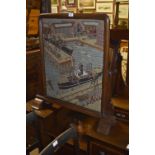 An early 20th century carved oak fire screen set with woolwork tapestry depicting a harbour scene