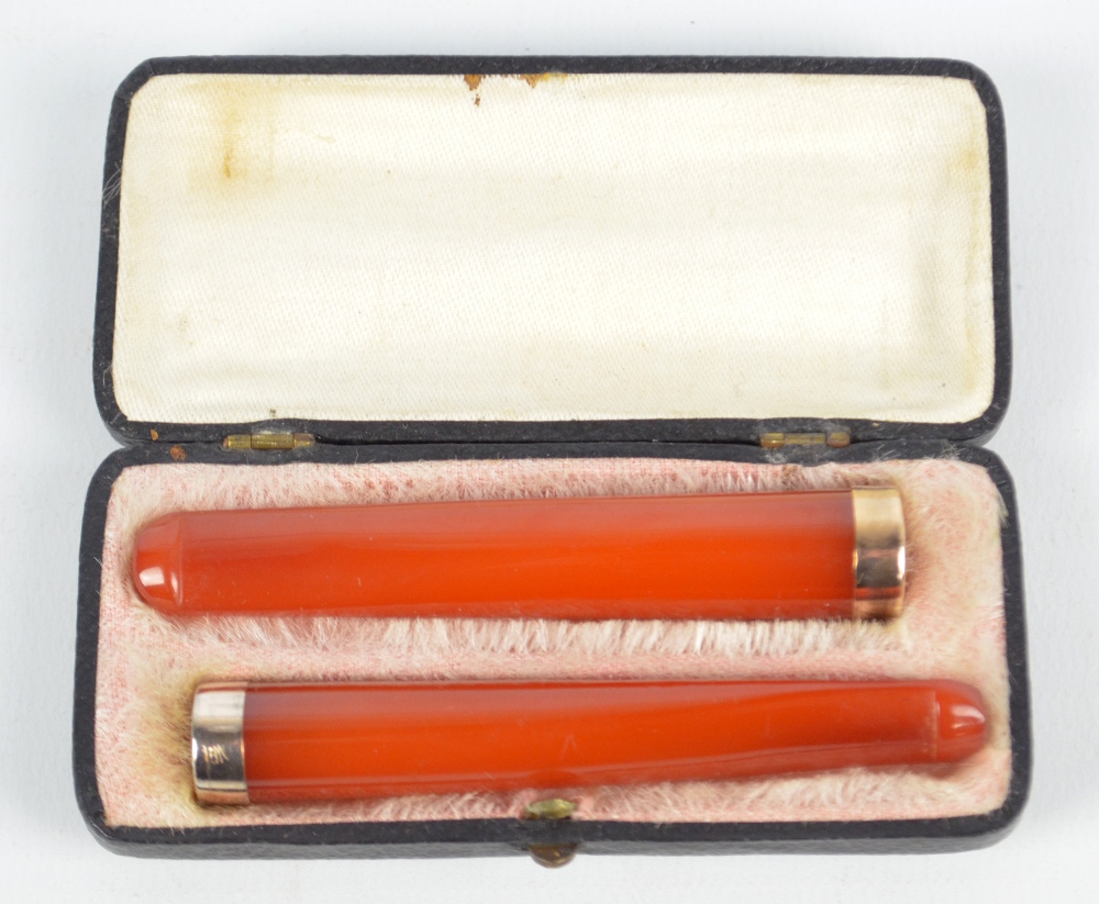 A cased pair of amber coloured cheroot holders, each with bands stamped '18K'.