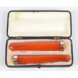 A cased pair of amber coloured cheroot holders, each with bands stamped '18K'.