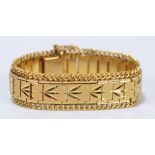 A yellow metal bracelet with engraved central band and with safety chain,