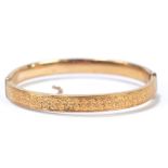 A 9ct yellow gold hinged bangle with engraved detail to one half (safety chain af), approx 9g.