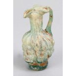 A Roman green glass mold-blown flask decorated with a young male head; long thin neck, handgrip