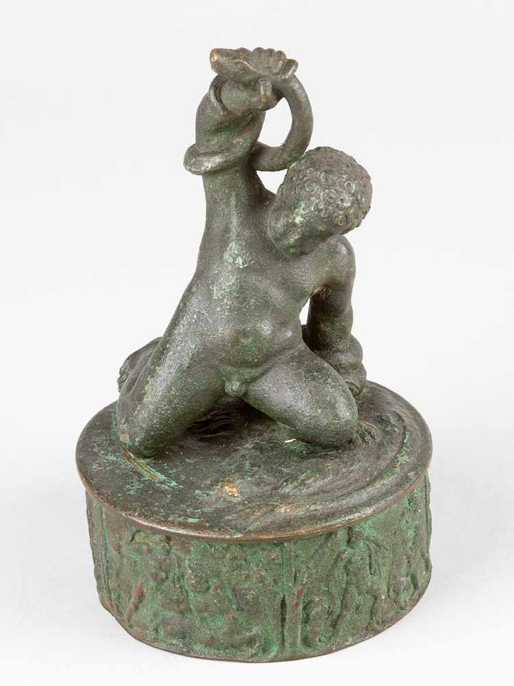 A bronze box in Roman style, round form with casted ancient ornaments, on top boy fighting with