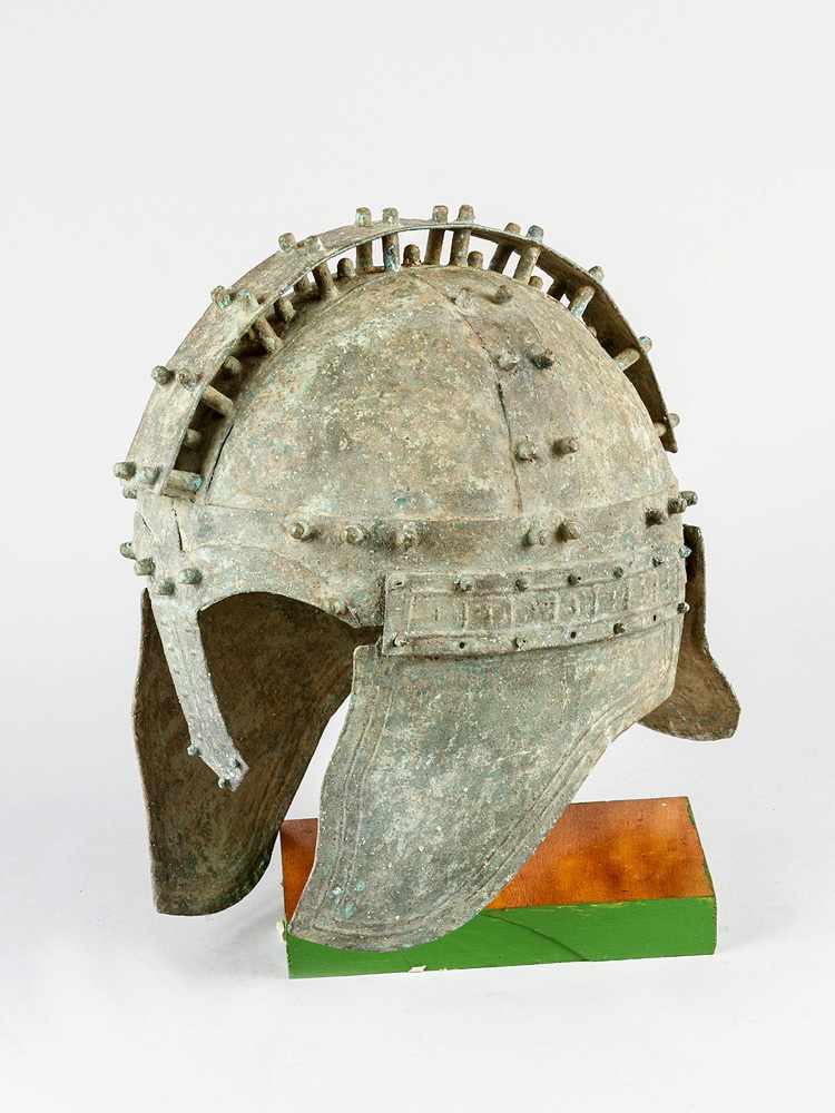 A bronze or copper warrior helmet in ancient Greek or Mediterranean style; the helmet with decorated