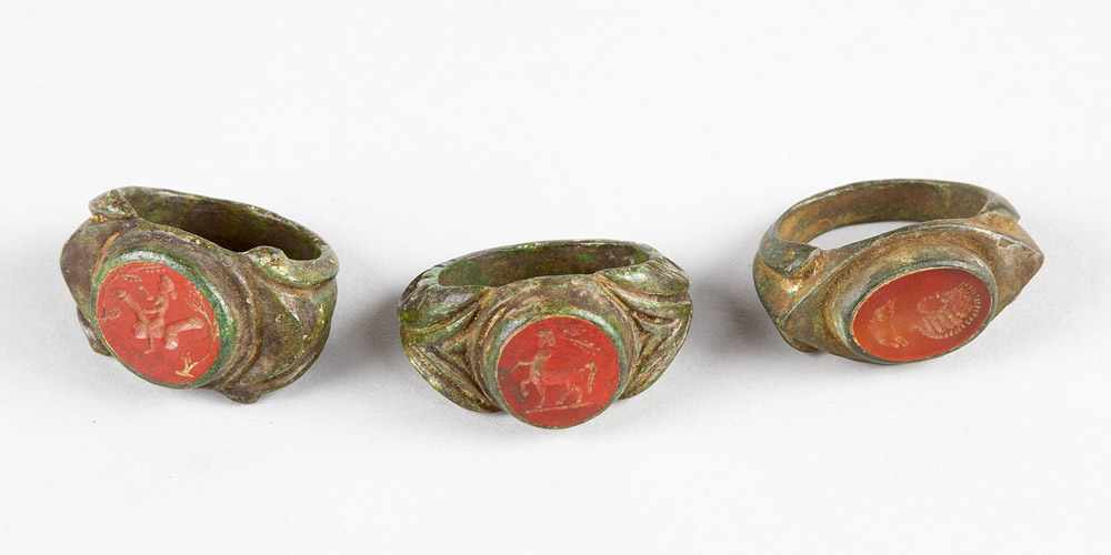 Set of three Roman bronze rings with red gemstones showing a portrait, a centaur and an erotic