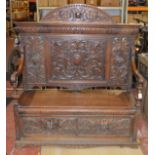 An oak settle bench with intricately carved design and paneling.