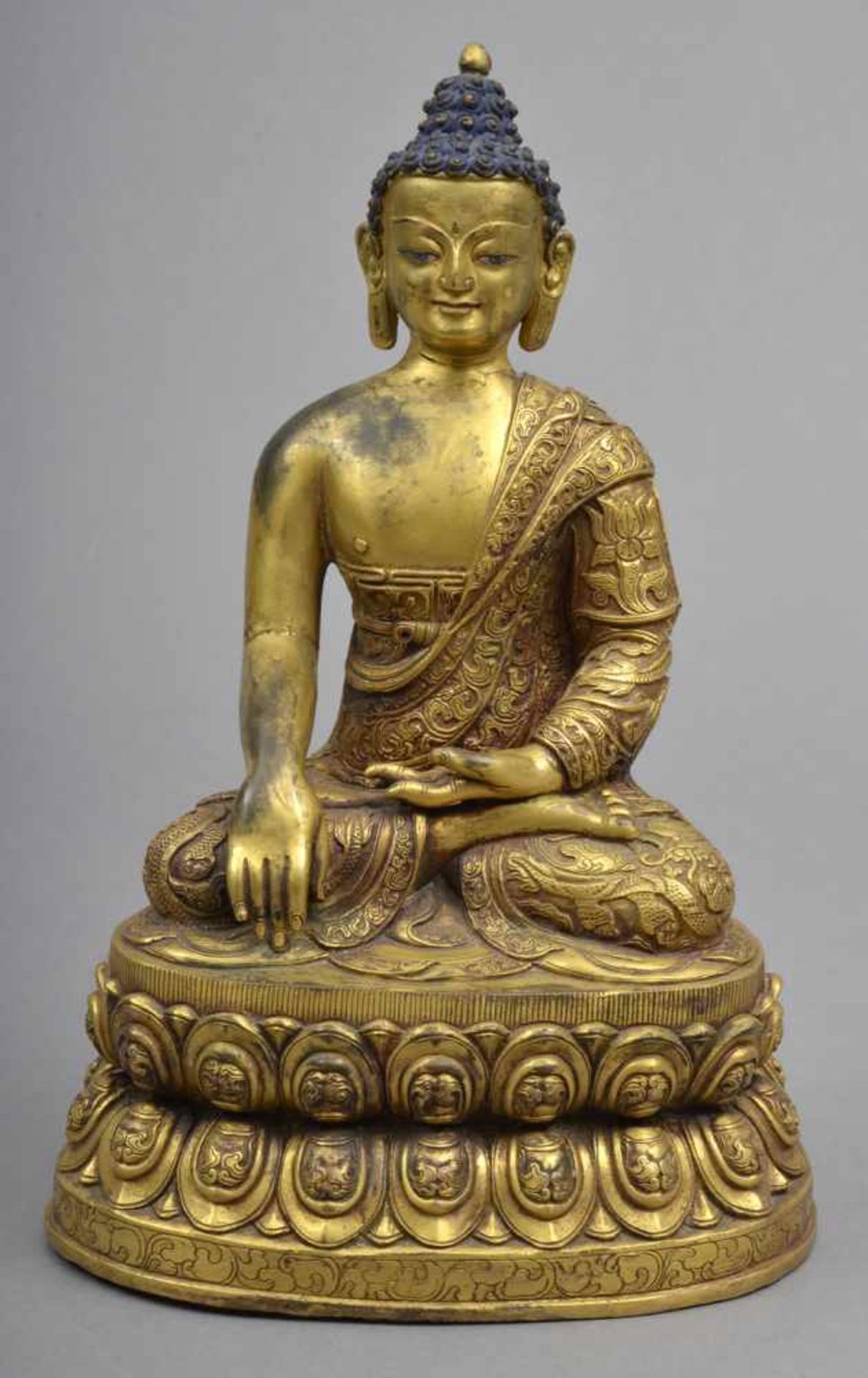 Buddha Sakyamuni in aufwendig ziseliertem Mönchsgewand auf ebensolchem doppelten Lotosthron.