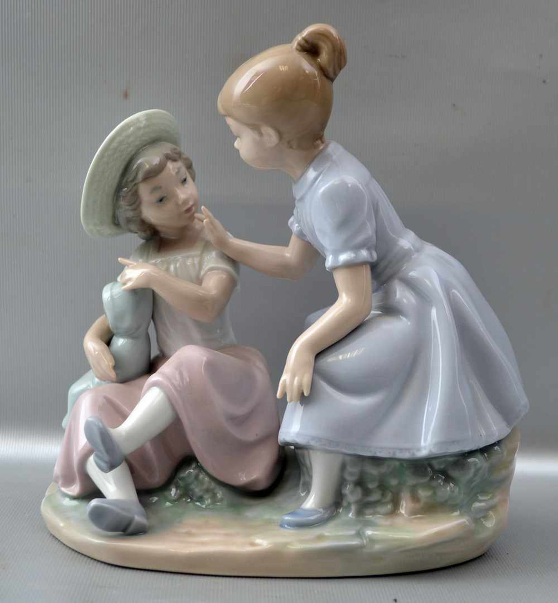 Zwei spielende Mädchen auf Steinsockel sitzend, mit Puppe, bunt bemalt, H 18 cm, B 18 cm, FM Lladro