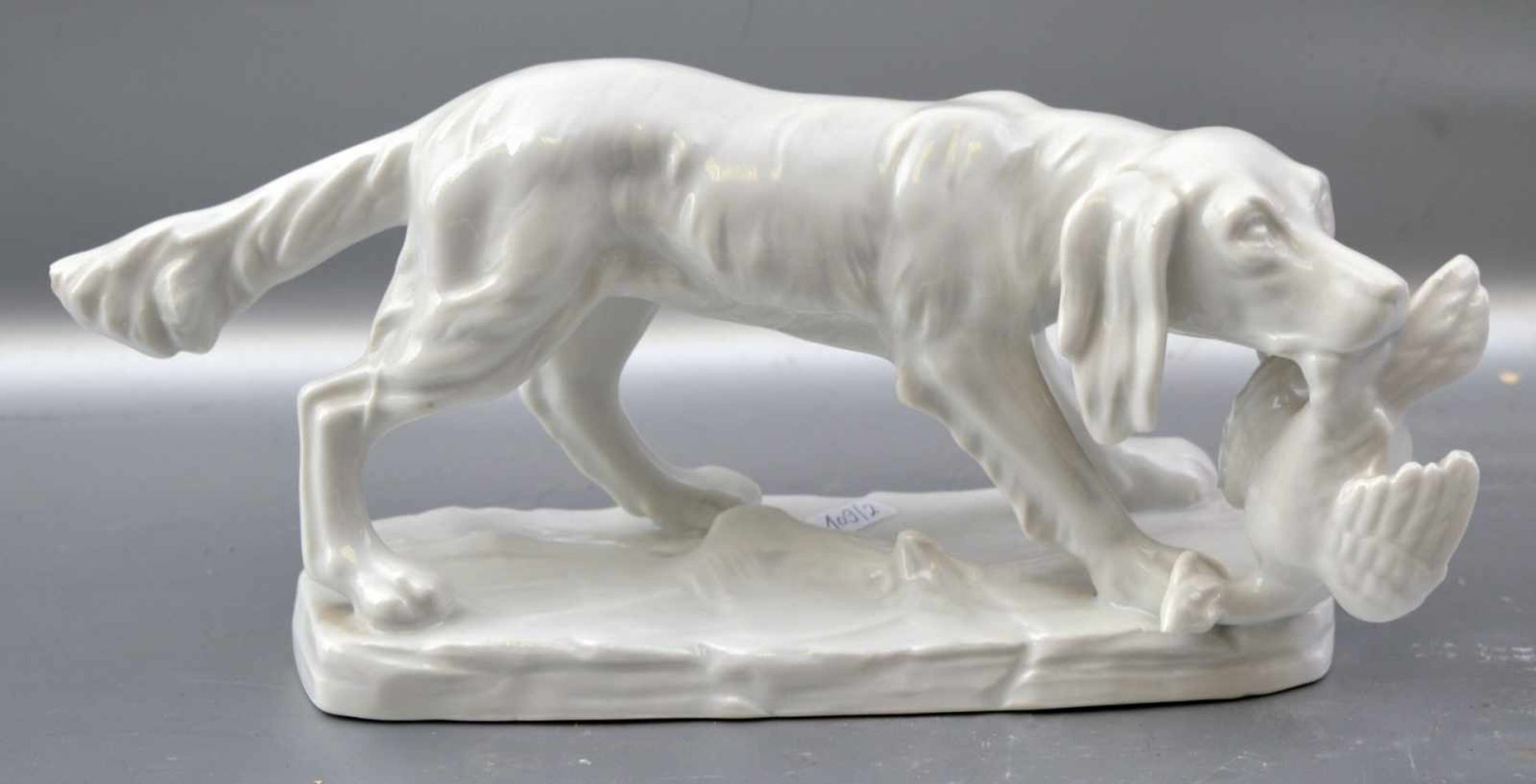 Jagdhund auf Sockel stehend, weiß glasiert, mit apportierter Ente, leicht best., H 10 cm, L 25 cm,