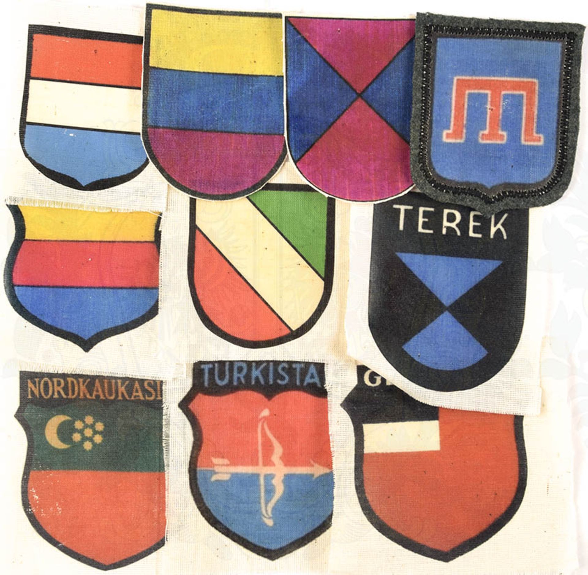 10 ÄRMELABZEICHEN F. OSTLEGIONEN, weißes Tuch m. farb. Aufdruck in Wappenform, 1x auf feldgr.