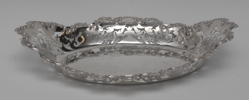 An Edwardian silver navette shaped cake dish, wavy border pierced and embossed with C-scrolls,