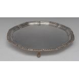 A George III style silver shaped circular salver, plain field, gadrooned border, wrapped knurl feet,