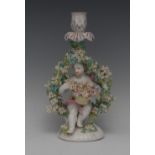 A Derby figural candlestick, of a scantily clad cherub, seated holding a basket of flowers,